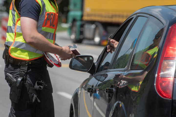 Ein Polizeibeamter kontrolliert an der Grenze die Ausweise der Autoinsassen.