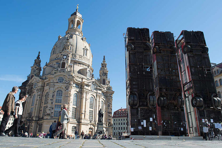 Passanten betrachten die drei aufrecht aufgestellten, ausrangierten Linienbussen, die zusammen das Kunstwerk "Monument" des syrischen Künstlers Manaf Halbouni ergeben.