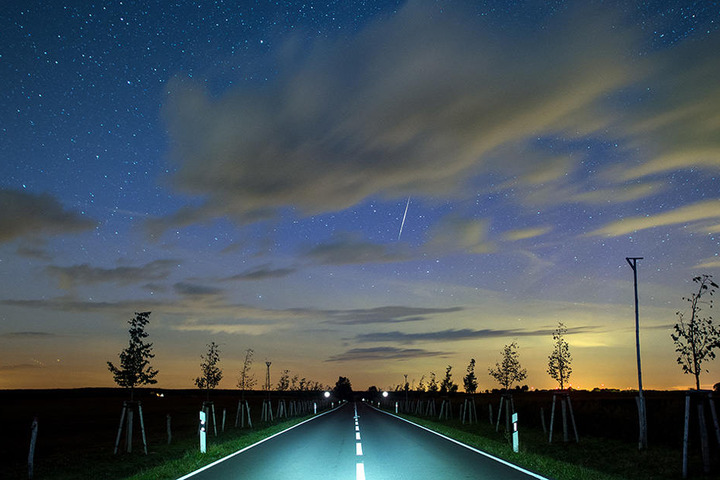 Eine Sternschnuppe leuchtet am Nachthimmel über eine Landstraße nahe Lietzen im Landkreis Märkisch-Oderland (Brandenburg).
