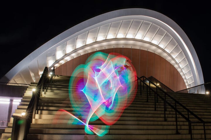 Ort der Festlichkeiten: Ein Mann zeichnet mit einem Lichtstab vor dem Haus der Kulturen der Welt Muster in den Abendhimmel.
