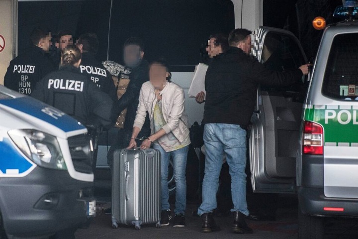 In Handschellen schiebt ein Mann seinen Koffer.