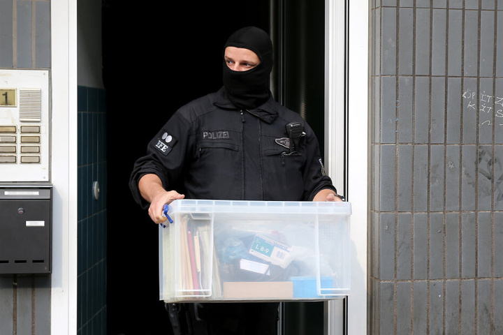 Ein Bundespolizist verlässt ein Wohnhaus mit sichergestelltem Material.
