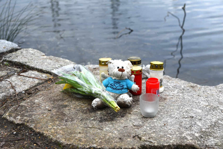 Jemand hat Kerzen, Blumen und ein Stofftier am Ufer des Weihers abgelegt.