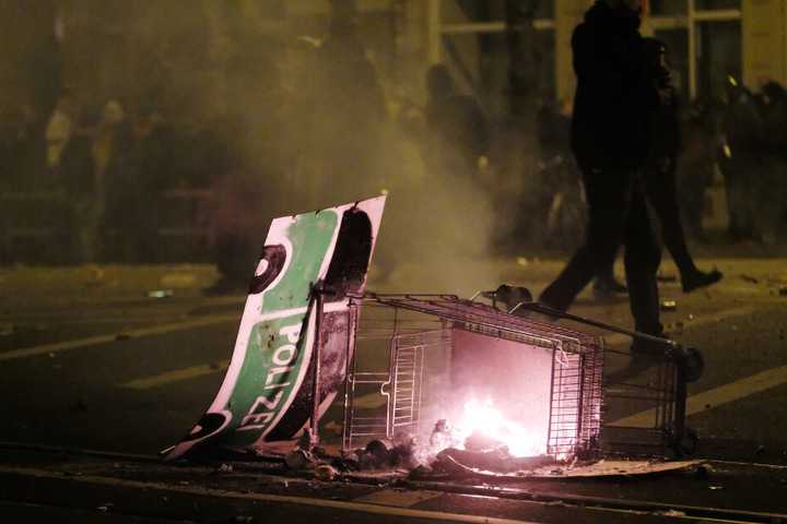 An dem brennenden Einkaufswagen hing ein auf eine Pappe gemaltes Polizeifahrzeug.