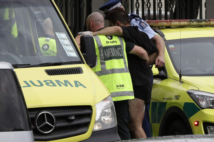 Ein Polizist und Rettungskräfte helfen einem Verwundeten außerhalb einer Moschee.