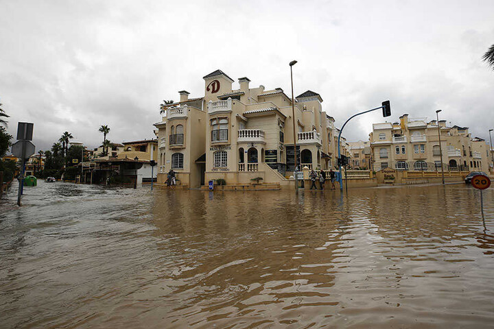 Menschen gehen nach Unwettern und Regenfällen eine überflutete Straße von Torrevieja entlang.