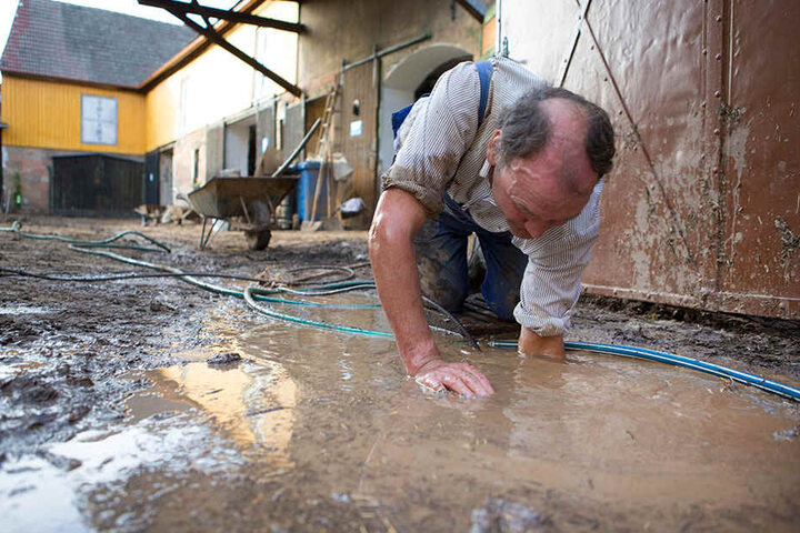 Ein Anwohner versucht nach dem starken Unwetter in Bad Bibra mit einem Gartenschlauch einen Regenabfluss zu entstopfen. Hagelkörner so groß wie Hühnereier zerschossen die Regenrinnen und die Schlammmassen durchbrachen das Tor.