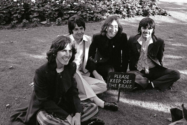 George Harrison, Paul McCartney, John Lennon und Ringo Starr sitzen auf einer Wiese.