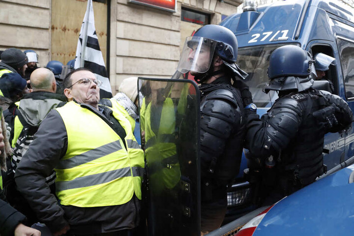 Demonstranten mit gelben Westen werden von Polizisten beim Betreten eine Straße in Paris aufgehalten.