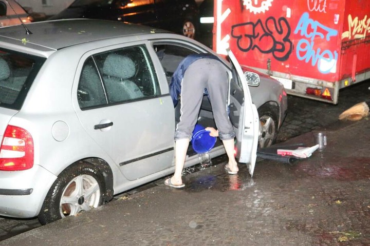 Auto-Besitzer versuchen ihre Wagen mit Eimern von den großen Wassermengen zu befreien.