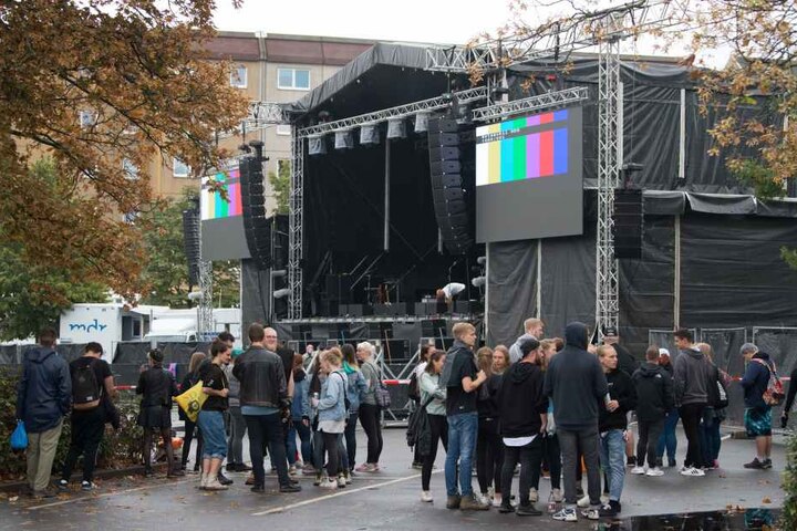 Konzertbesucher warten auf dem Parkplatz an der Johanniskirche hinter einer Absperrung vor der Bühne.