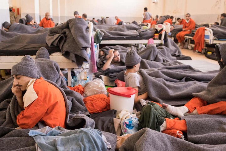 Zahlreiche Männer in orangenen Overalls sitzen und liegen in einem Raum.