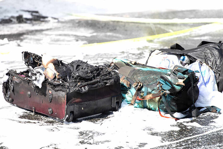 Taschen und Koffer liegen verkohlt neben dem Brandfahrzeug.