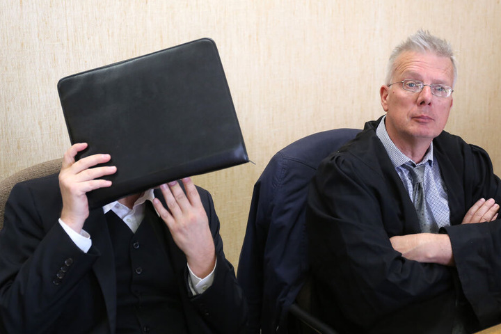 Der Angeklagte hält sich im Amtsgericht neben seinem Anwalt Konrad Schäfer (r) eine Aktentasche vor das Gesicht.