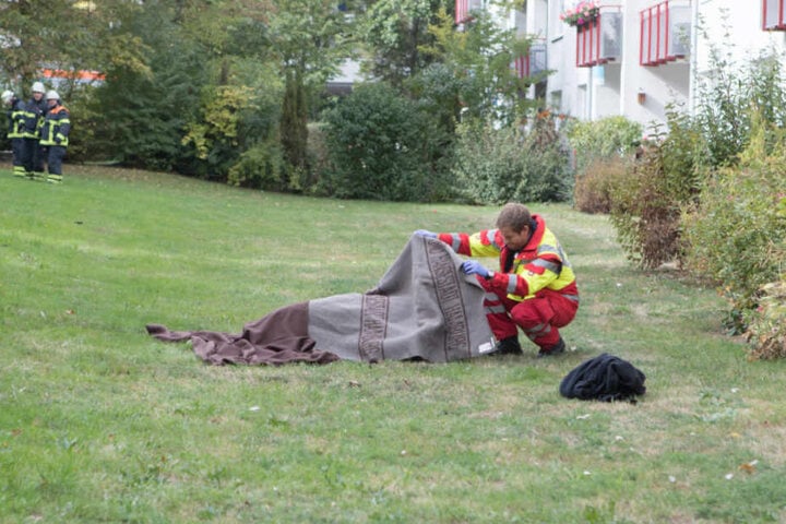 Unter einer Decke der Feuerwehr liegt das 50-jährige Opfer auf dem Rasen.
