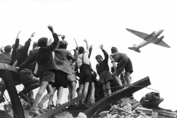 30.11.1947, Berlin: Das Foto aus dem Jahr 1948 zeigt West-Berliner Jungen, die auf einem Trümmerberg stehen, und einen US-amerikanisches Transportflugzeug, das Versorgungsgüter nach West-Berlin bringt, winken.
