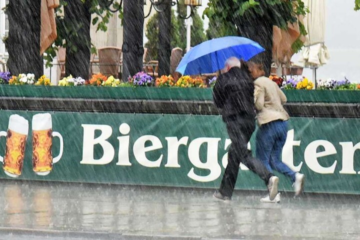 Ein Pärchen flüchtet unter dem Regenschirm aus einem Biergarten.