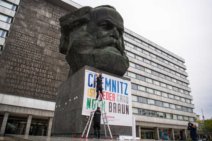 Zwei Männer befestigen am Karl-Marx-Denkmal ein Plakat mit der Aufschrift "Chemnitz ist weder grau noch braun". (Archivfoto)