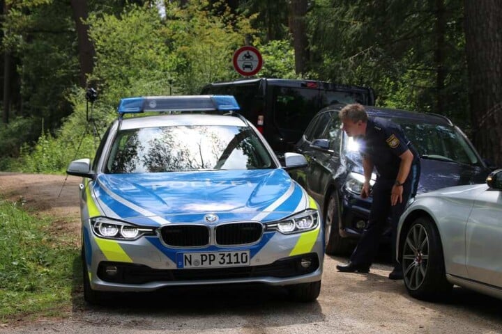 Ein Polizist steht auf einem Waldweg an einem Einsatzfahrzeug der Polizei. In einem Wald im Landkreis Nürnberger Land ist ein toter Mann gefunden worden. Die Kriminalpolizei hat die Ermittlungen aufgenommen.