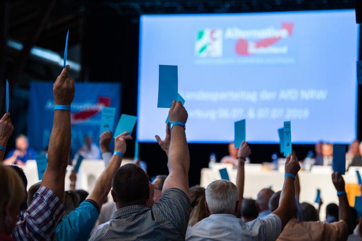 Delegierte halten beim Landesparteitag der NRW-AfD bei einer Abstimmung ihre Stimmzettel hoch.