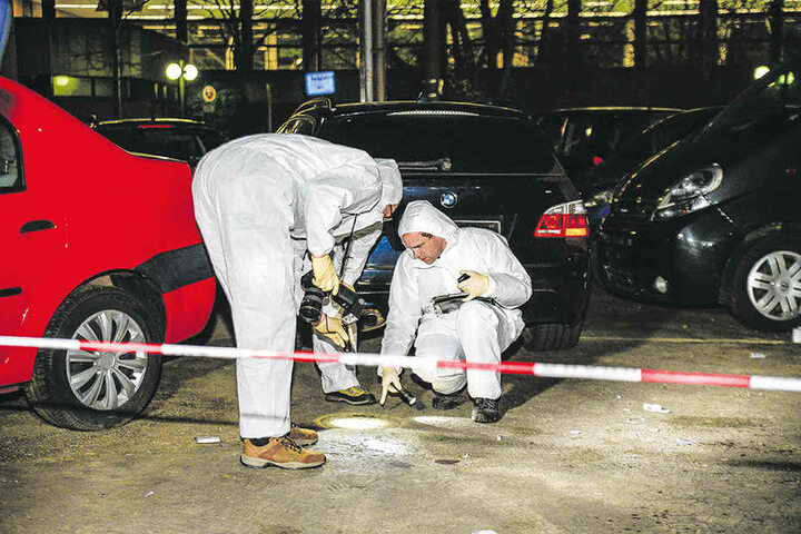 Zwei Beamte sind mit der Spurensicherung auf dem Parkplatz beschäftigt.