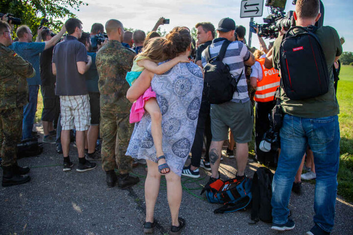 Eine Einwohnerin von Jabel mit einem Kind auf dem Arm verfolgt die Presseerklärung der Bundesverteidigungsministerin in der Nähe der Absturzstelle eines Eurofighters.
