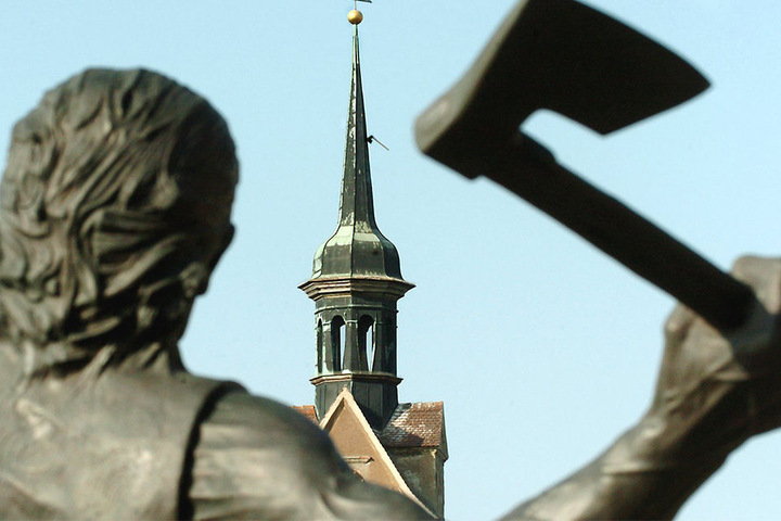 Diese Bronzefigur mit Beil in der Hand steht in Mockrehna. Im Hintergrund ist der Turm der Dorfkirche zu sehen.