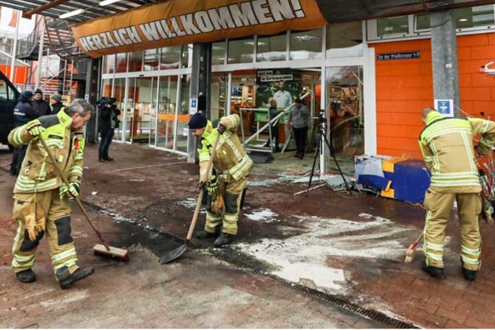 Feuerwehrmänner beseitigen die Brandspuren vor dem Baumarkt.