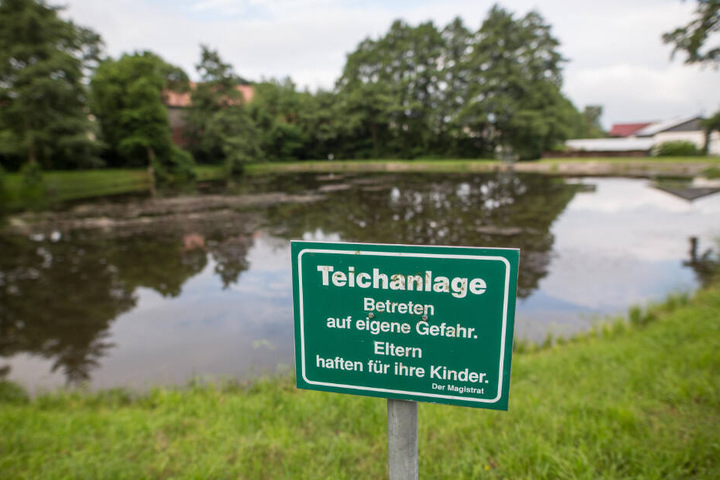 Ein Schild mit der Aufschrift "Teichanlage Betreten auf eigene Gefahr. Eltern haften für ihre Kinder." weist auf eine Teichanlage hin.