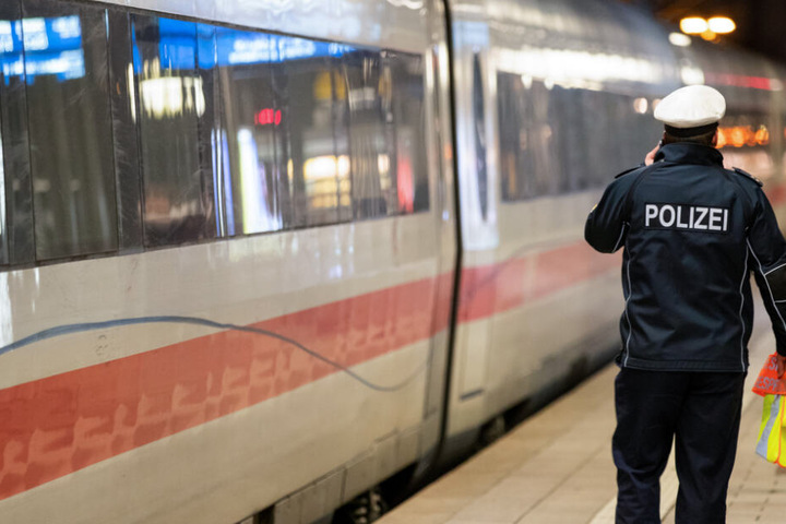 Ein ICE steht im Hauptbahnhof einer deutschen Großstadt, während daneben ein Polizeibeamter telefoniert.