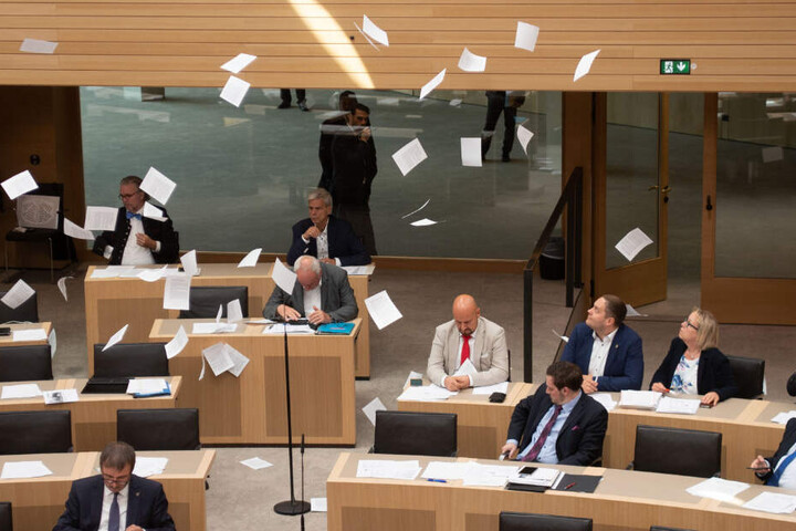 Die Abgeordneten sitzen im Landtag, während Flugblätter auf sie rieseln.