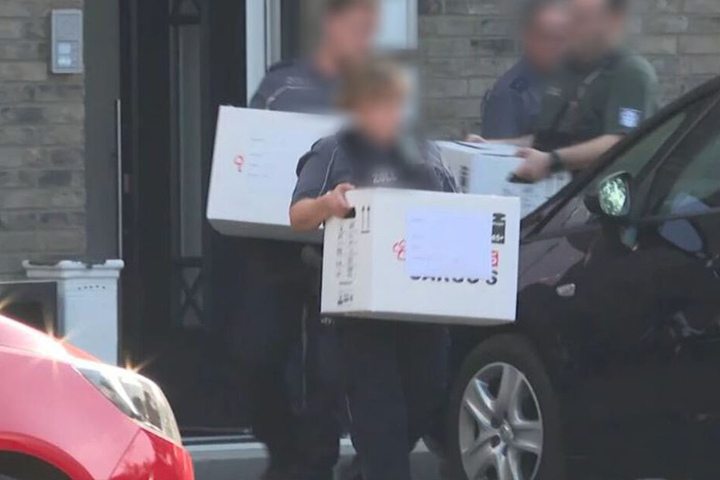 Zollbeamte tragen beschlagnahmtes Material aus einem Haus.