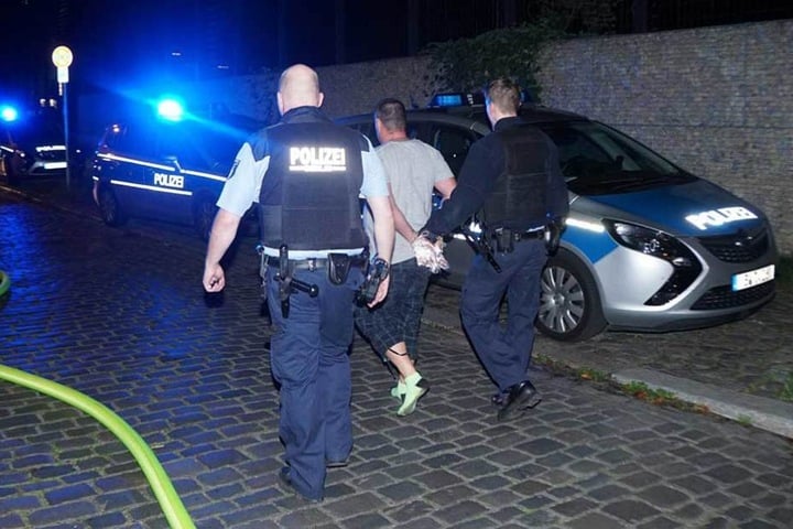 Polizisten führen den Verhafteten ab und bringen ihn zum Auto.