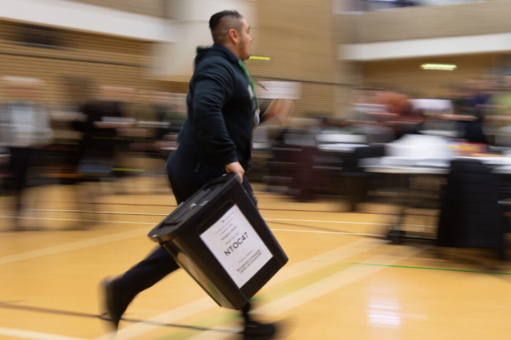 Mit einer Wahlurne in der Hand spurtet ein Wahlhelfer durch das Lokal.