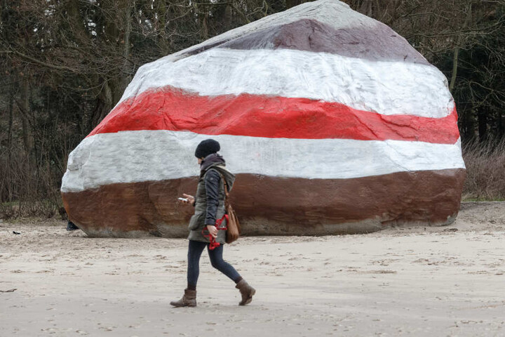 Eine Fußgängerin läuft am Elbstrand vor dem neu bemalten Findling entlang.