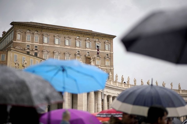 Menschen stehen unter Regenschirmen auf dem Petersplatz, um den Segen von Papst Franziskus zu empfangen.