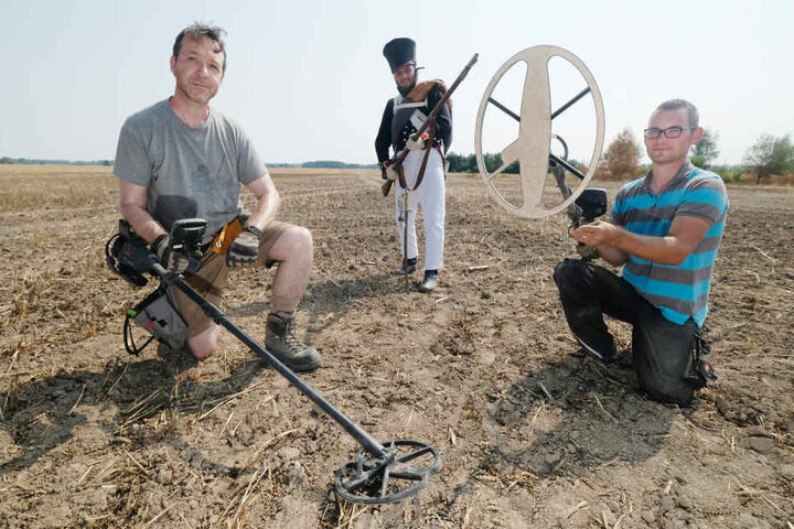 Michael Cahill (l.) und Michael Schmahl (r.) suchen auf einem Acker in Leipzig-Holzhausen nach Überbleibseln von vor über 200 Jahren. Dahinter posiert Michel Kothe in preußischer Uniform.