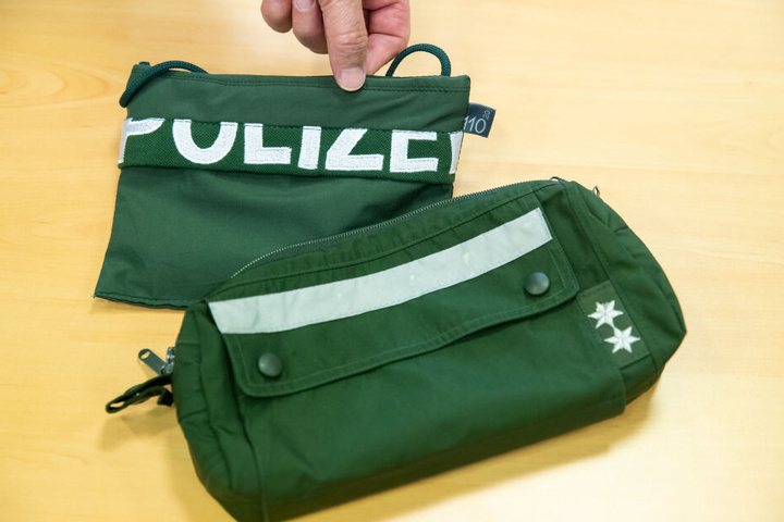 Ein Brustbeutel und eine Fahrrad-Lenkertasche gefertigt aus Stoffen alter Polizei-Uniformen liegen auf einem Tisch.