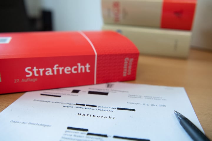 Eine Abschrift eines Haftbefehls liegt mit einem Strafrecht-Buch und einem Kugelschreiber auf dem Tisch.