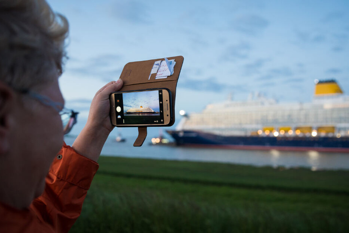Eine Frau verfolgt die Fahrt des Schiffs und macht ein Foto des Kreuzfahrtriesens mit ihrem Smartphone.