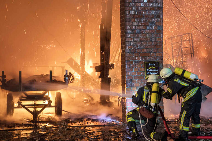 Feuerwehrleute spritzen Wasser in die brennende Scheune.