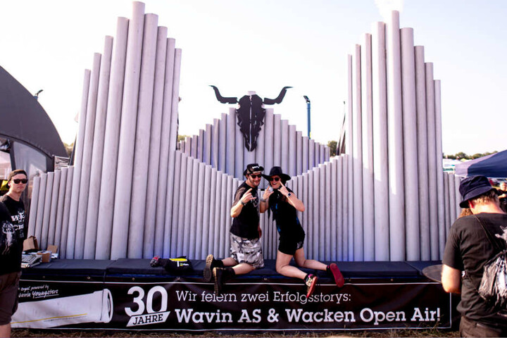 Zwei Wacken-Besucher lassen sich vor einer Holz-Skulptur fotografieren.