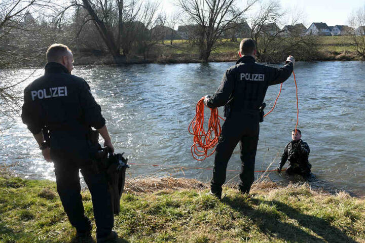 Polizeikräfte unterstützen einen Taucher, der den Uferbereich absucht.