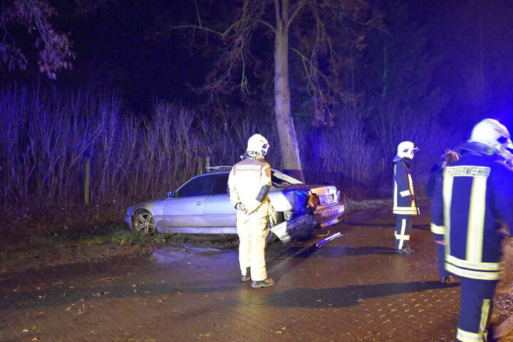 Einsatzkräfte der Feuerwehr stehen vor dem beschädigten Auto