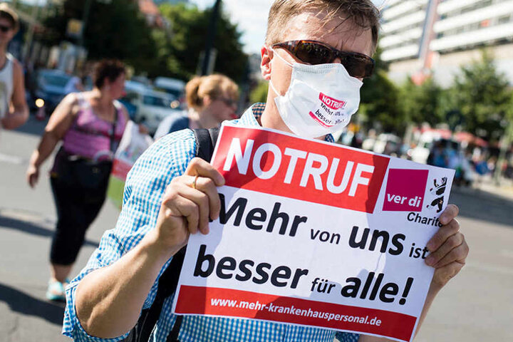 Pfleger Raimund trug am 30.06.2015 bei einer Kundgebung des streikenden Pflegepersonal der Charite in Berlin einen Mundschutz und ein Schild mit der Aufschrift "NOTRUF - Mehr von uns ist besser für alle!".