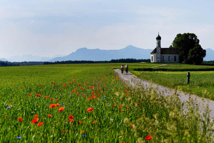 Herrliches Wetter am Samstag in Bayern: Radler fahren auf die St. Andreas Kirche zu, dahinter ist das Ammergebirge und das Wetterstein zu sehen.
