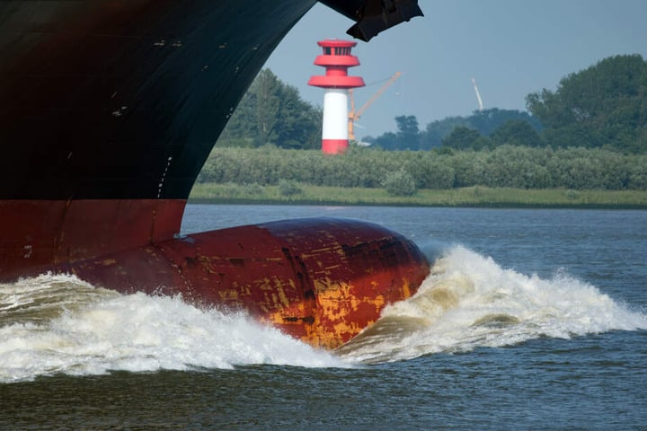 Der Bug eines Containerfrachters schiebt vor der Hafeneinfahrt in Hamburg eine große Welle vor sich her.