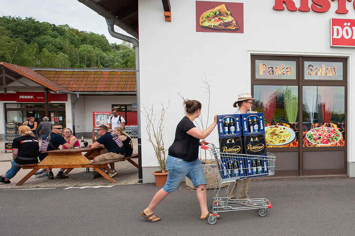 Eine Frau und ein Mann schieben einen Einkaufswagen mit Bier die Straße entlang.