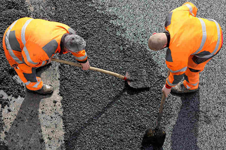 Zwei Straßenbauer flicken ein Schlagloch mit dem Kaltasphalt.
