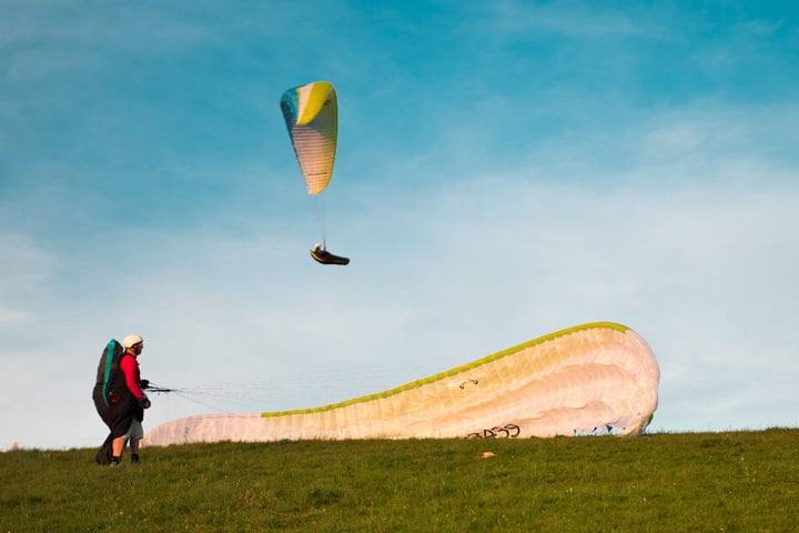 Auf einer Wiese ist ein Fallschirmspringer gelandet, ein weiterer setzt zur Landung an. (Symbolbild)